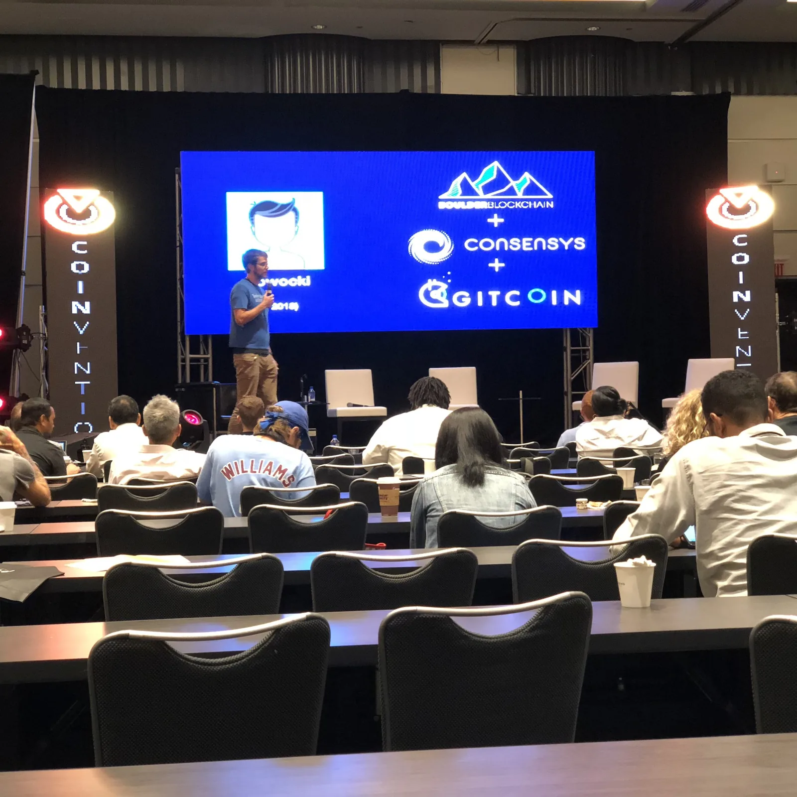 Speaker on stage at Coinvention in front of a slide with the Boulder Blockchain, ConsenSys and Gitcoin logos